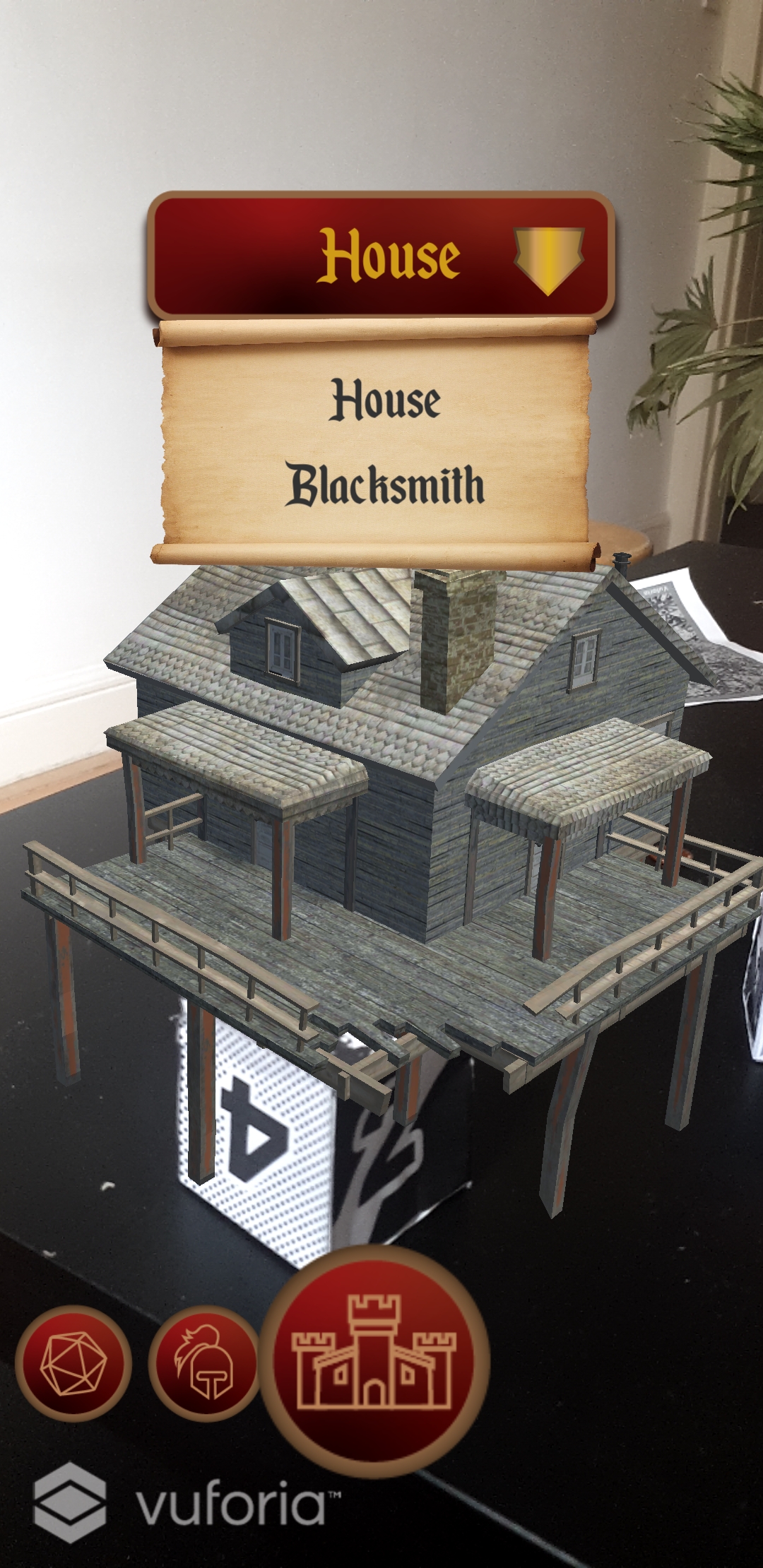 Photograph of dice with 3d model of a house projected to the top of it. UI shows enlarged centre circle button with a castle icon, and two smaller circle buttons with icons of armor and a dice. Dropdown shows parchment scroll with options House and Blacksmith